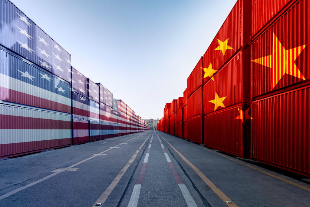 A road surrounding by shipping containers. On the left side are shipping containers that mimic the American/U.S. flag and on the right are shipping containers that mimic the Chinese flag.